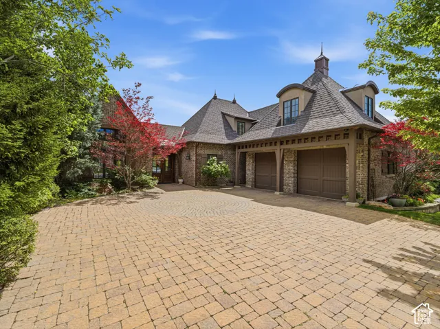 Stone and stucco exterior featuring a multi-car garage with wood-finish doors, a turret, and a paver driveway