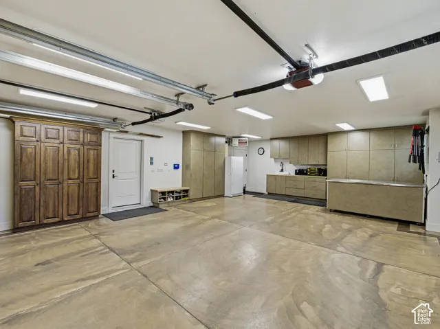 Spacious garage featuring a durable concrete floor, extensive built-in cabinetry, overhead lighting fixtures, and a white entry door
