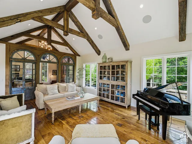 Vaulted ceiling with exposed wood beams, wood-finish flooring, and multiple large windows