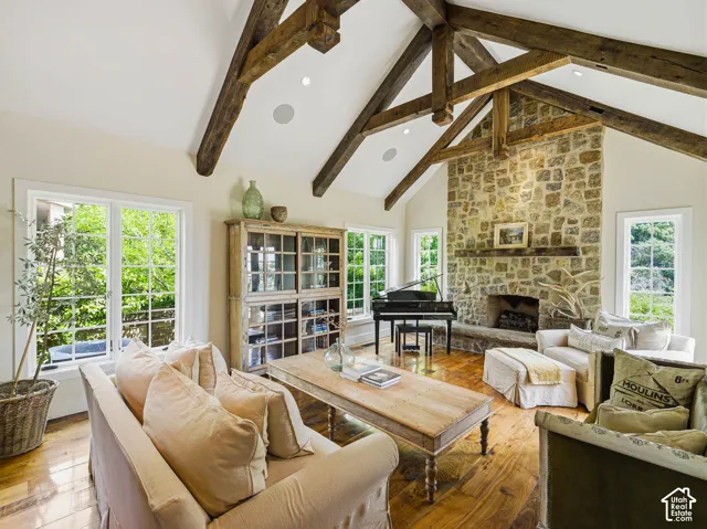Spacious living area featuring a vaulted ceiling with exposed wood beams, a stone-clad fireplace, and multiple grid-pattern windows