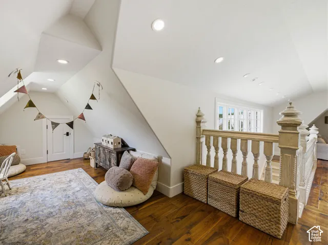 Upper level space featuring rich wood-finish flooring, a painted spindle railing, bright recessed lighting, a white paneled door, and a multi-pane window