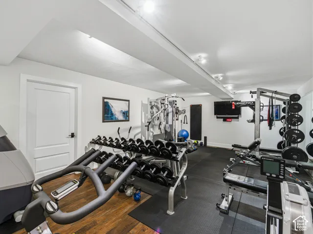 Dedicated fitness space featuring rubberized flooring and a wood-finish flooring section, recessed lighting, and a mounted flat-screen display
