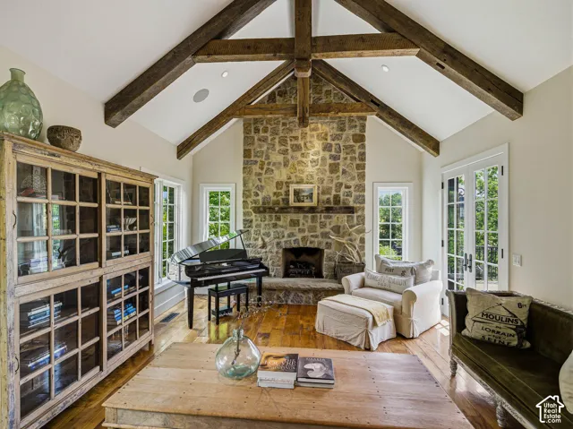 Spacious living area featuring exposed wood beams, a stone fireplace, wood-finish flooring, recessed lighting, and French doors