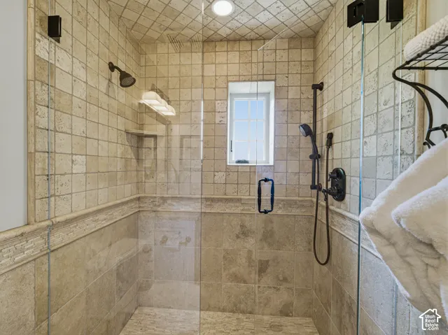 Tiled shower enclosure featuring a clear glass door, oil-rubbed bronze fixtures, a recessed window, and a built-in shower niche