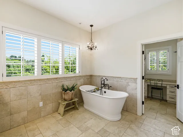 Freestanding soaking tub with a floor-mounted faucet, complemented by large format floor tiles and coordinating wall tile wainscoting