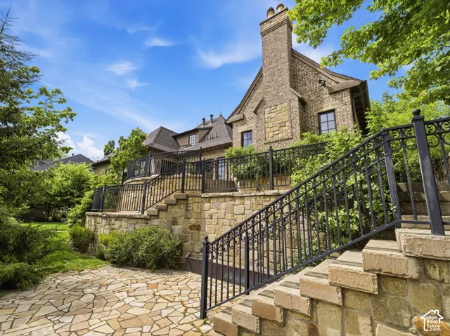 Stone and brick exterior with a prominent brick chimney, multi-level stone hardscaping, wrought iron railings, a stone patio, and dormer windows