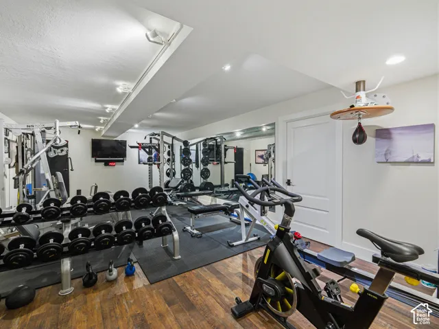 Dedicated fitness room featuring wood-finish flooring, recessed lighting, track lighting, and a white paneled door