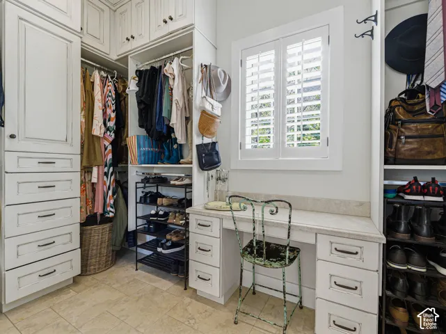 Custom-designed closet system featuring built-in cabinetry, upper storage, open shelving, and a dedicated vanity with a stone countertop