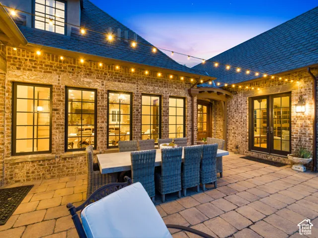 Spacious paver patio featuring string lighting, multiple black-framed windows, and double French doors with transom windows