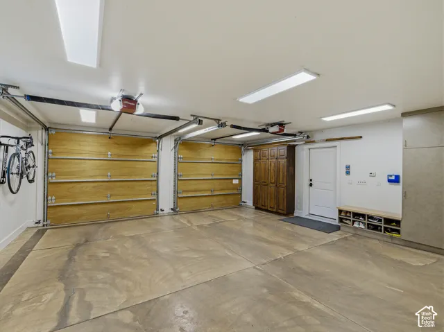 Spacious garage featuring a concrete floor, two wood-paneled garage doors with automatic openers, overhead fluorescent lighting, built-in wood cabinetry, and a white entry door