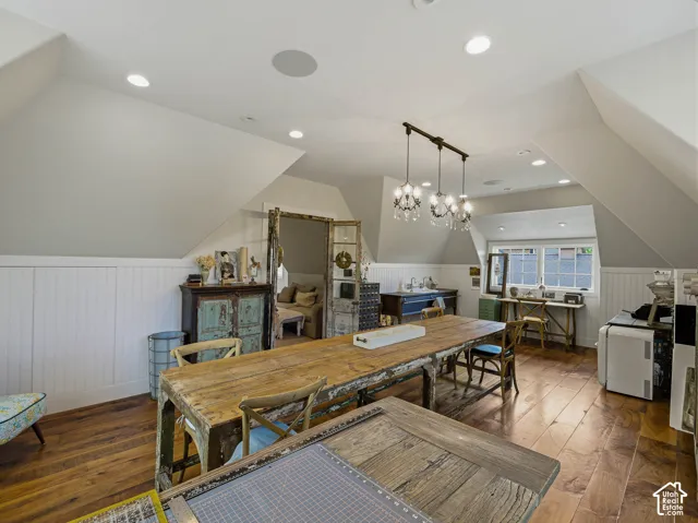 Spacious attic room featuring wood-finish flooring, white wainscoting, recessed lighting, and a multi-light chandelier