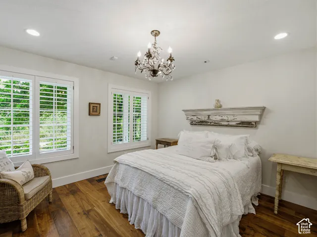 Room featuring wood-finish flooring, two large windows with white louvered shutters, a crystal chandelier, and recessed ceiling lighting