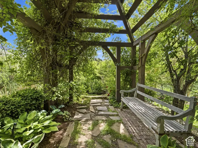 Wood pergola featuring climbing greenery, a stone slab pathway, and brick paver flooring