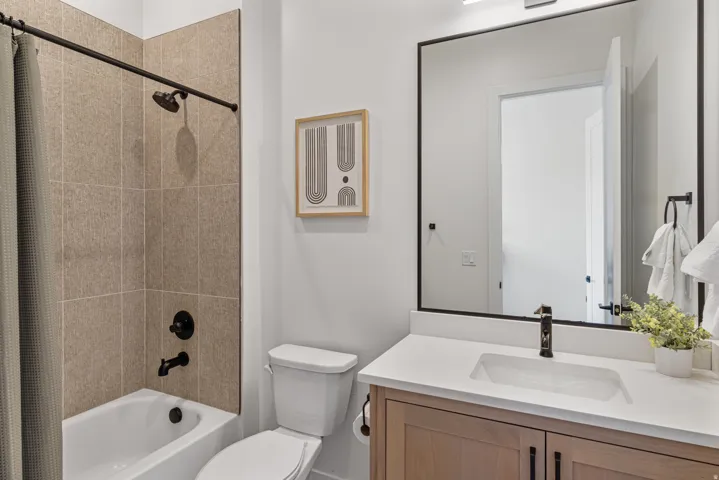 Bathroom featuring a light wood-finish vanity with a white countertop and integrated sink, a rectangular framed mirror, and a shower-over-tub combination with large format tiled walls and matte black fixtures