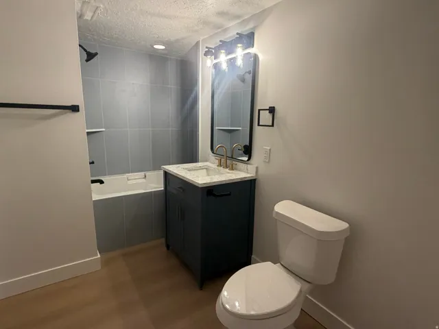 Basement level, full bathroom. Contemporary bathroom featuring a dark blue vanity with a light-toned countertop, a rectangular mirror, and a three-light fixture