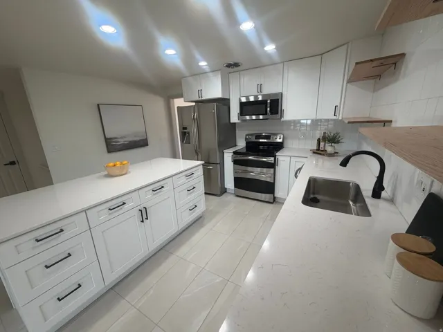 Bright kitchen featuring a large center island with integrated storage, white shaker-style cabinetry, stainless steel appliances, white subway tile backsplash, and light-toned tile flooring