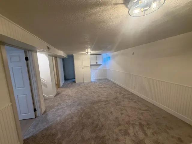 Spacious room featuring gray textured carpeting, white beadboard wainscoting, and white painted walls