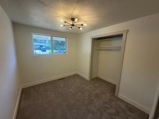 Bedroom 3. Bedroom featuring plush carpet flooring, a contemporary sputnik-style ceiling light fixture, a window with exterior visibility, a built-in closet with shelving and hanging rods, and perimeter base molding