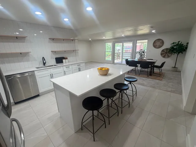Contemporary kitchen featuring a large center island with a stone-finish countertop, stainless steel appliances, white cabinetry, and a subway tile backsplash
