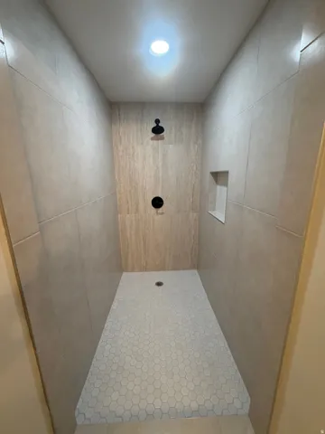 Master bathroom. Walk-in shower with hexagonal tile flooring, vertically stacked tile surround, built-in shelving, matte black fixtures, and recessed lighting
