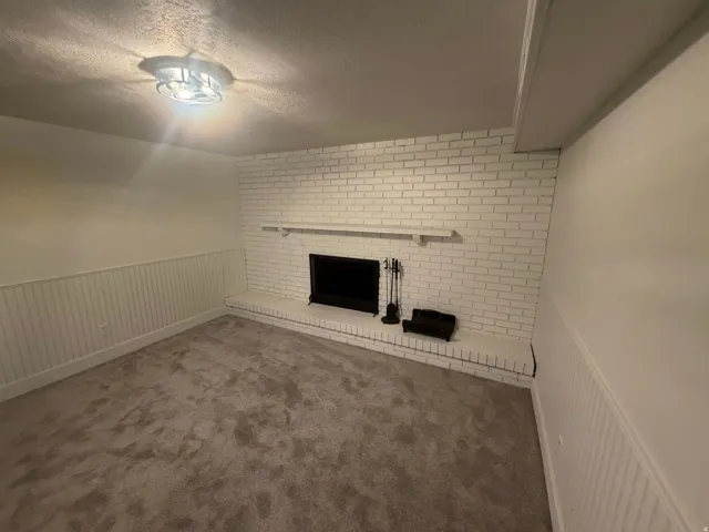 Living space featuring a white painted brick fireplace with a hearth, wall paneling, and neutral carpet flooring