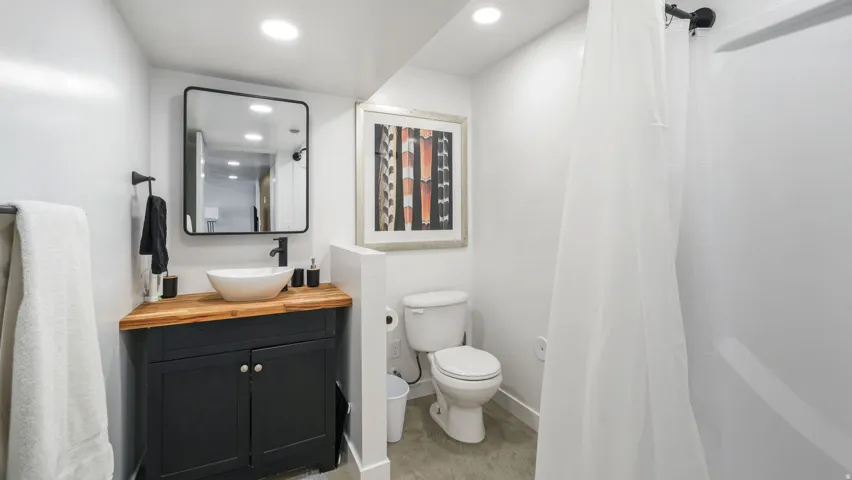 Full bathroom featuring a dark wood-finish vanity with a white vessel sink, a coordinating black-framed mirror, a toilet, and a shower with a white enclosure