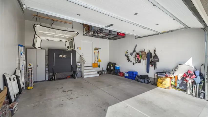 Spacious garage featuring concrete flooring, a white garage door, overhead storage racks, and finished white painted walls