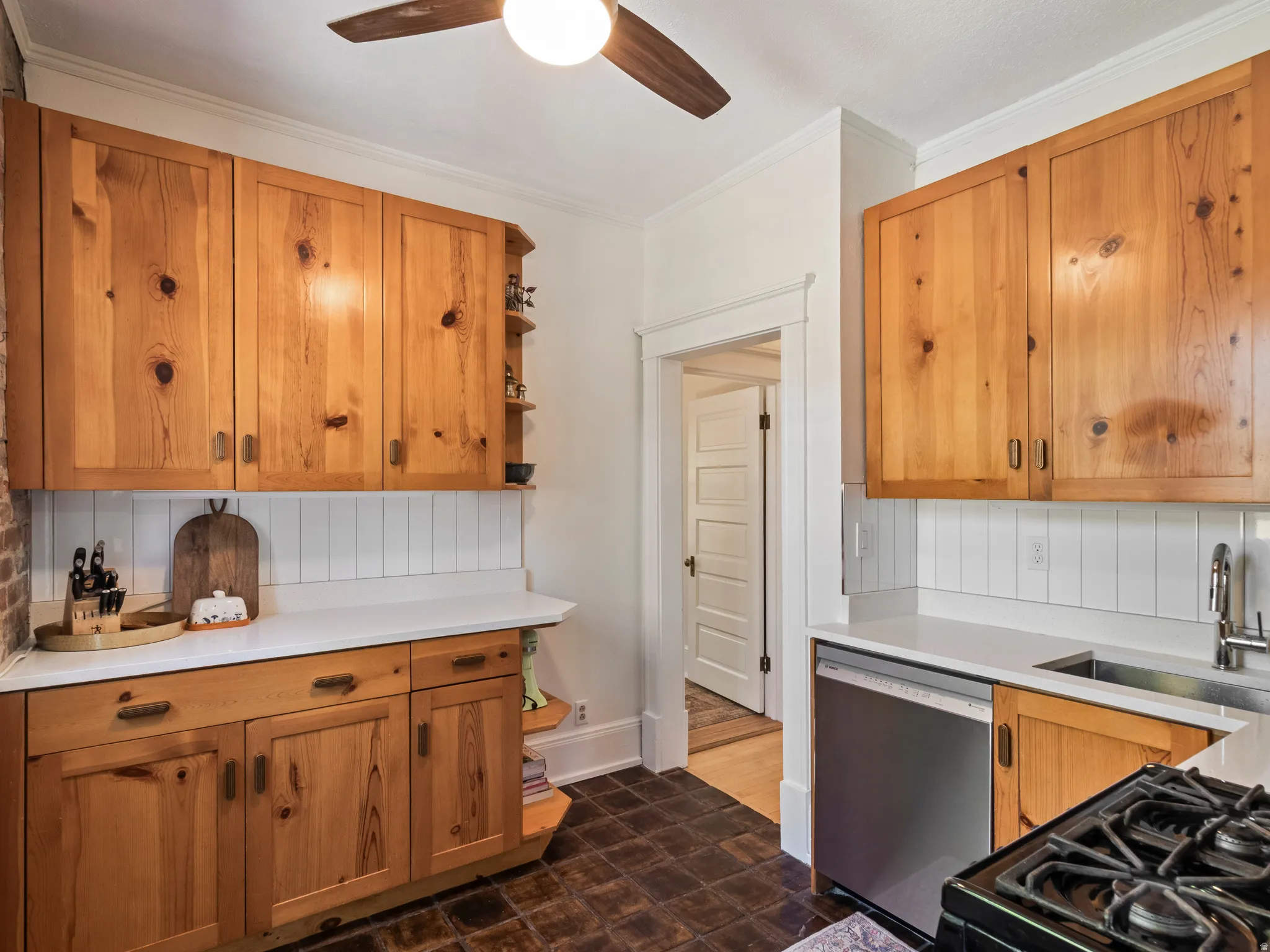 Kitchen featuring natural wood cabinetry, white countertops, white vertical panel backsplash, stainless steel appliances, and dark tile flooring