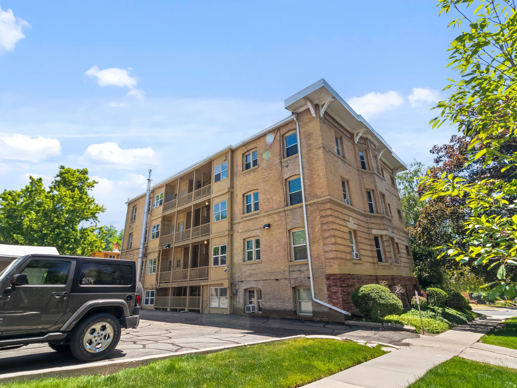 Brick multi-story building featuring multiple balconies, a stone foundation, and a side entrance