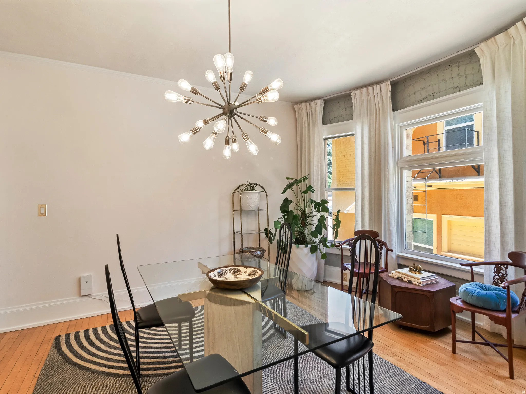 Dining area featuring a contemporary sputnik chandelier, light hardwood flooring, and multiple windows with white drapery
