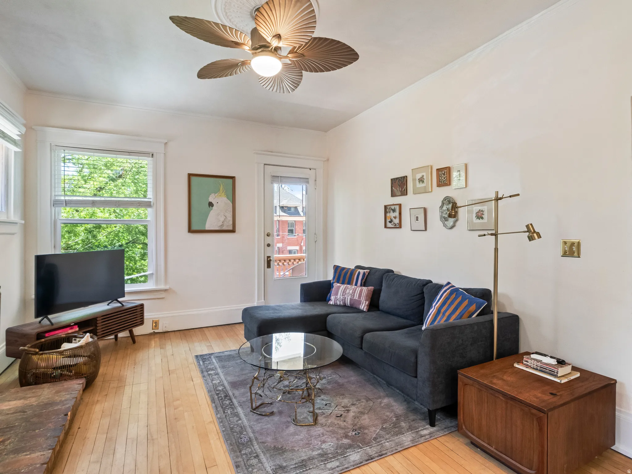 Living space featuring hardwood flooring, white trim, a ceiling fan with light fixture, and abundant natural light from multiple windows