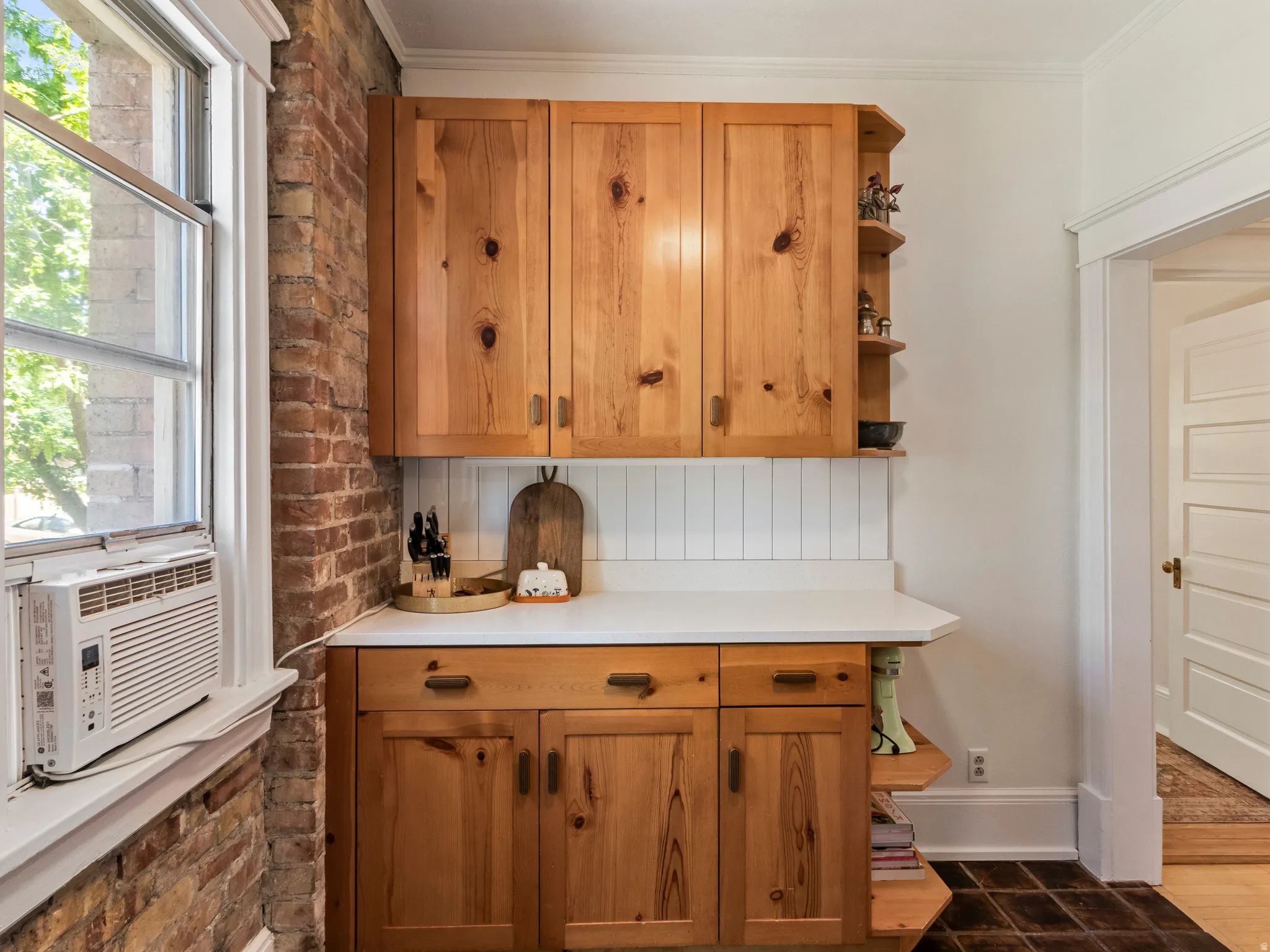 Natural wood-finish cabinetry featuring integrated shelving, white countertops, and a white beadboard backsplash