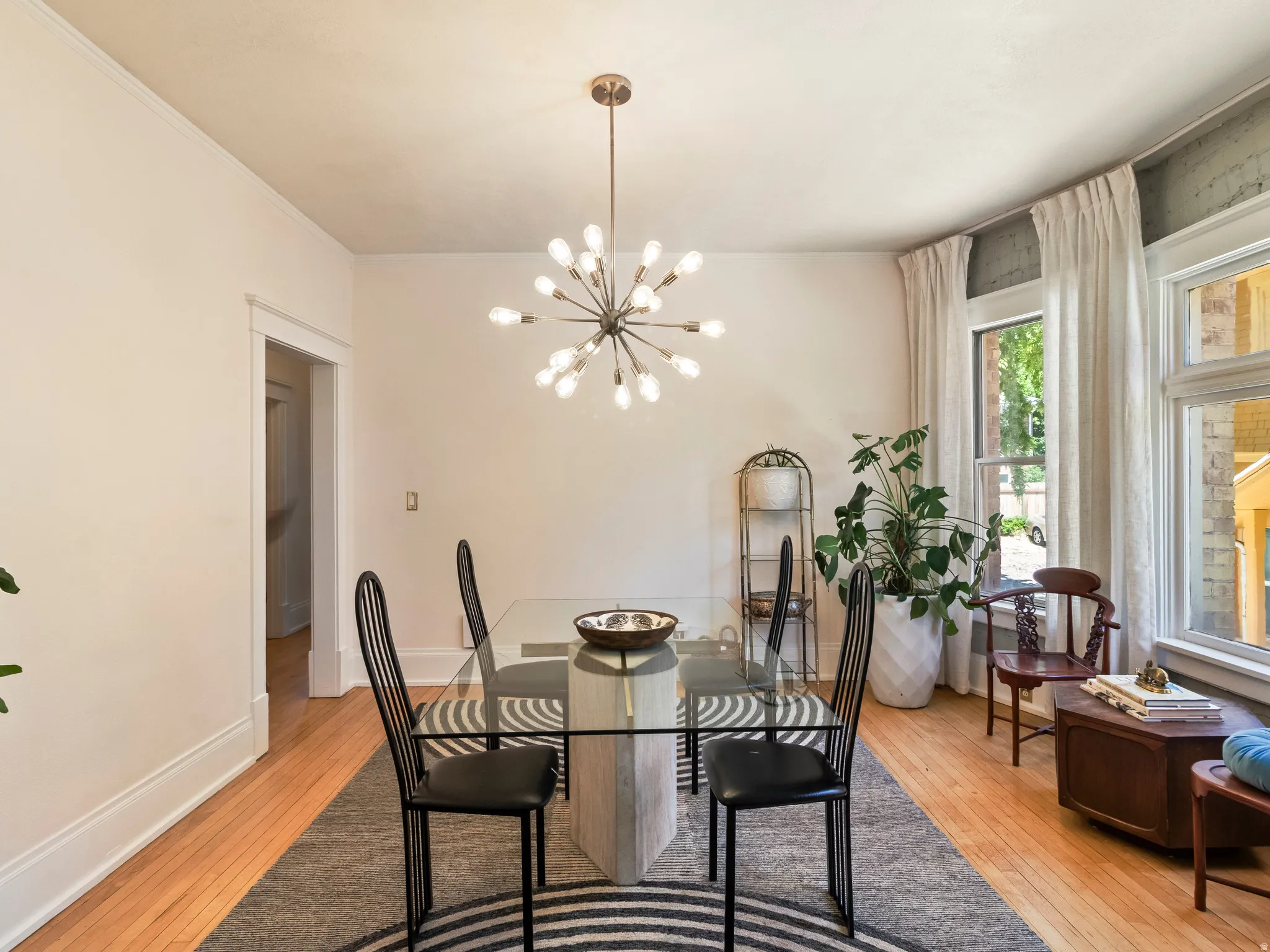Dining area featuring a contemporary sputnik chandelier, light hardwood flooring, and multiple windows with white drapery