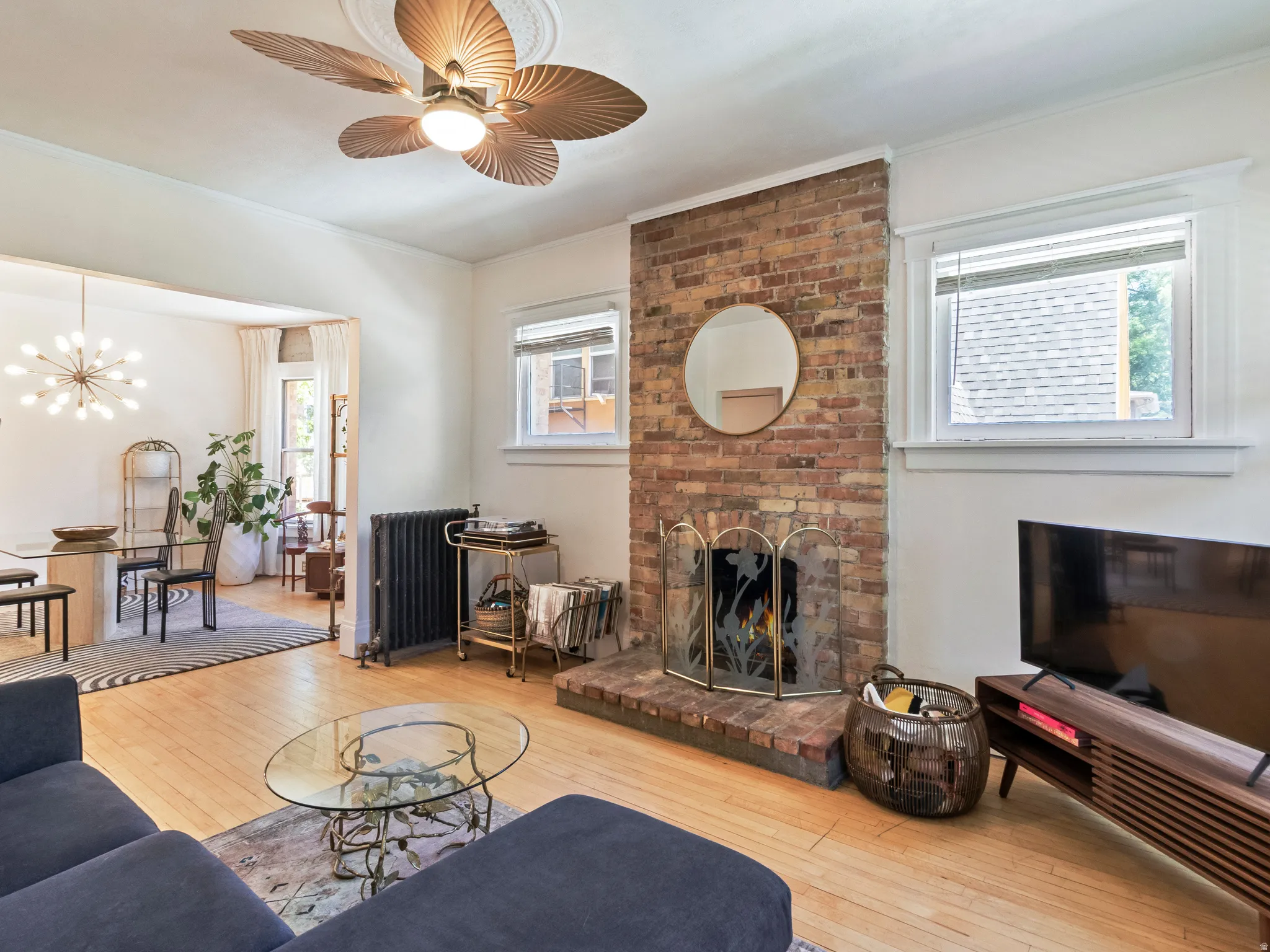 Living area featuring hardwood flooring, a brick fireplace, a decorative ceiling fan, and a radiator