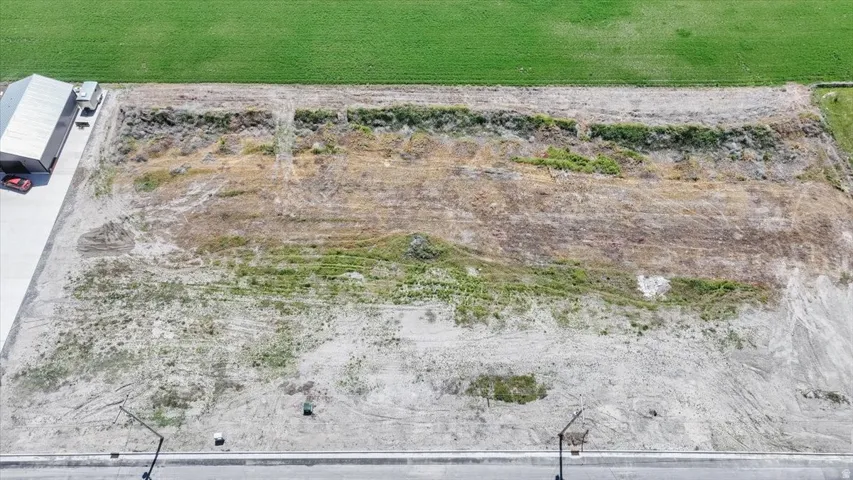 Expansive undeveloped lot featuring street frontage, adjacent paved areas, and proximity to green agricultural land