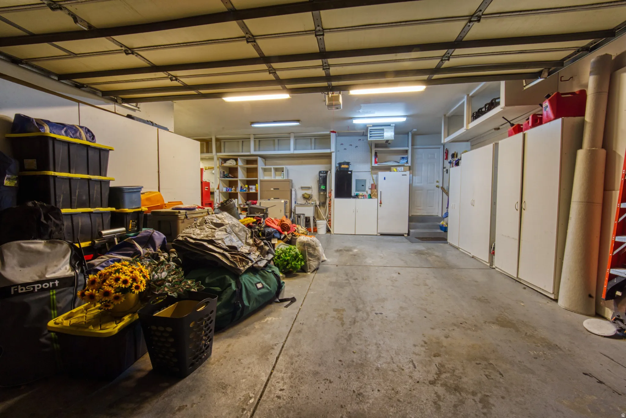 Spacious garage featuring concrete flooring, overhead fluorescent lighting, built-in shelving, and white cabinetry