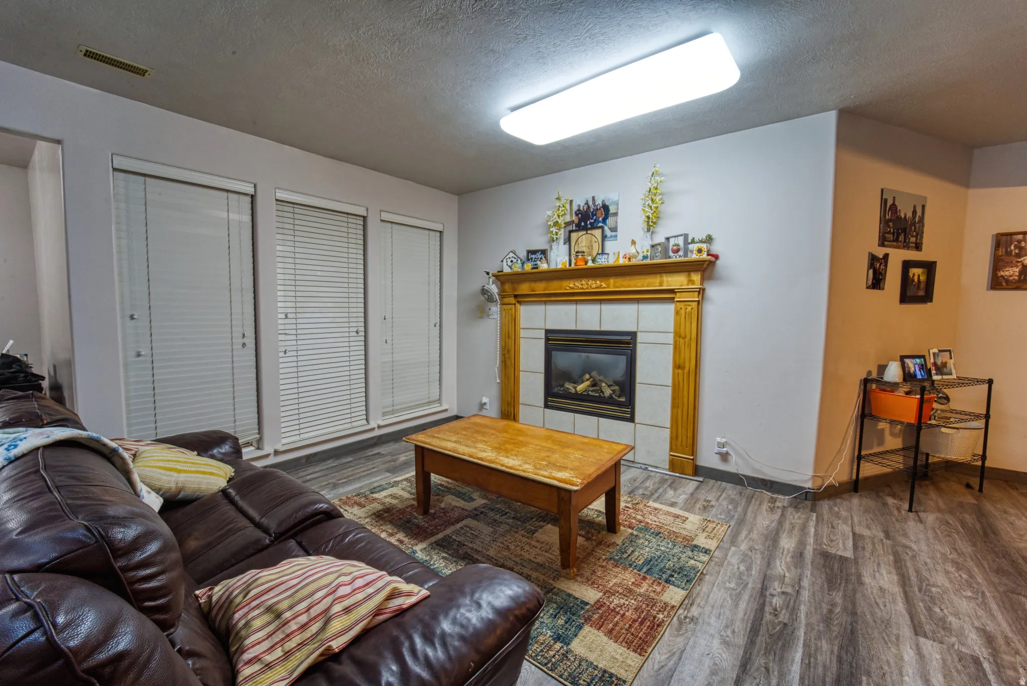 Living area featuring a gas fireplace with a tiled surround and wood mantel, wood-finish flooring, and recessed overhead lighting