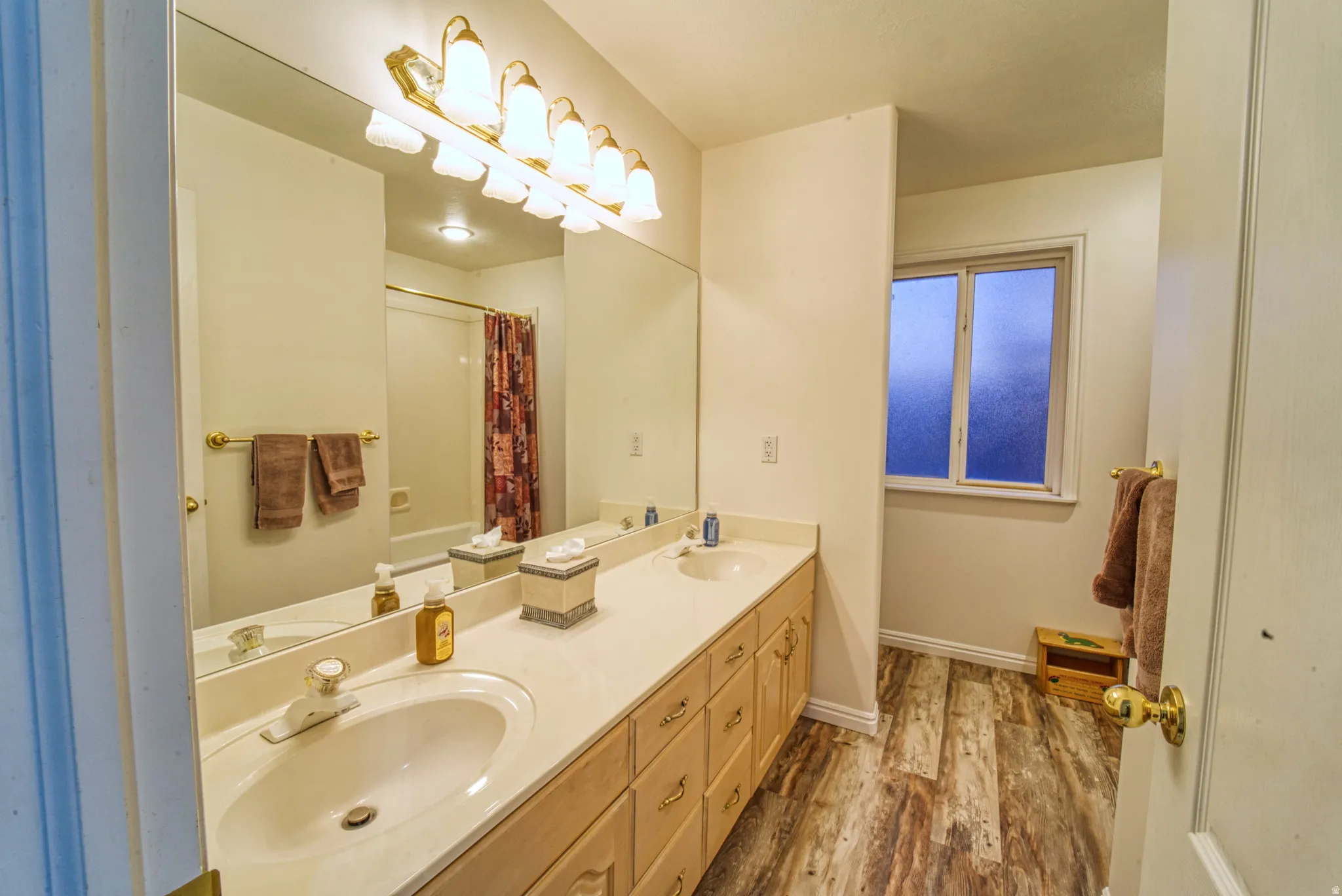 Double vanity with integrated sinks, ample countertop space, wood-finish flooring, and a frosted window
