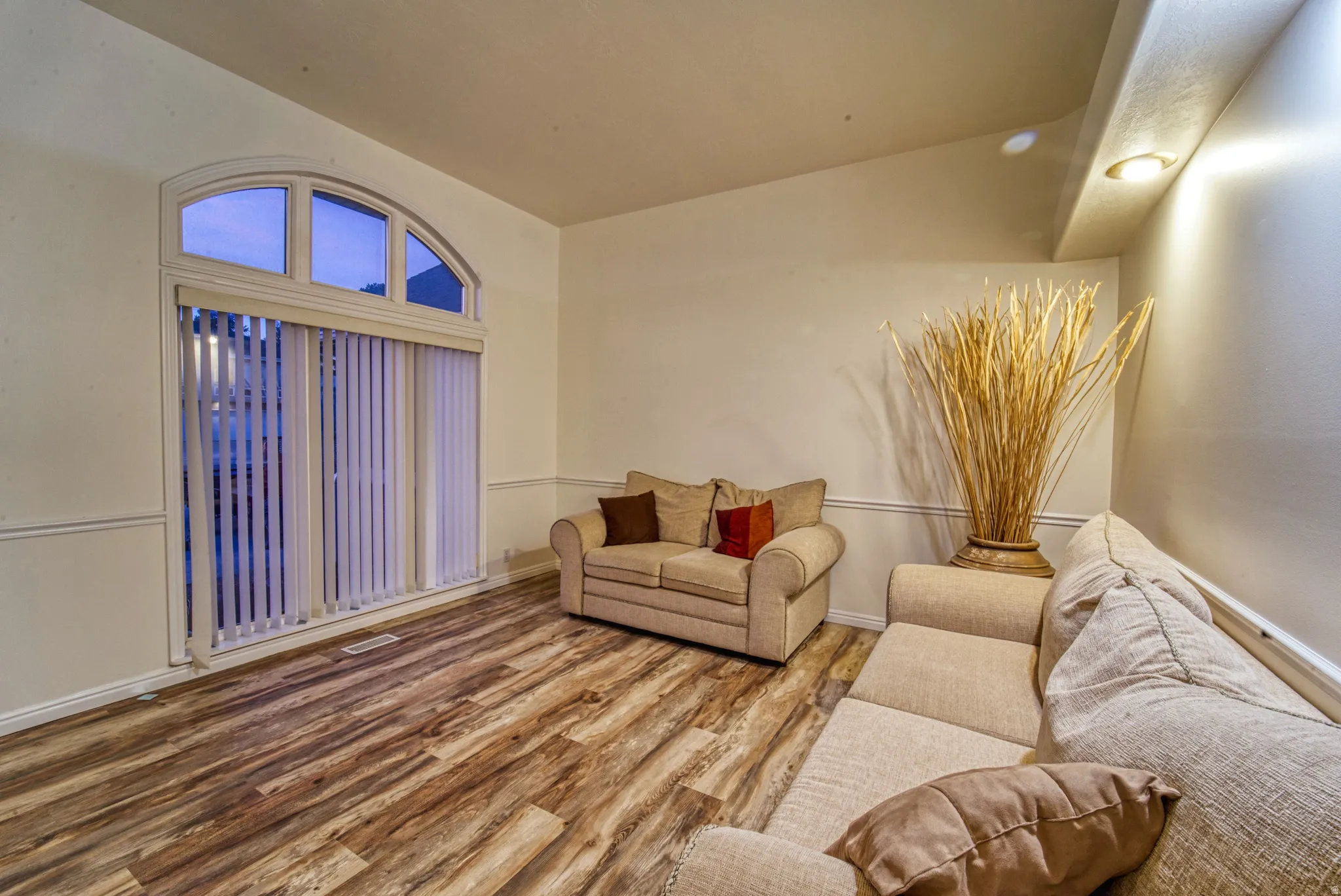 Living area featuring wood-finish flooring, an arched window with transom details, vertical blinds, and a chair rail