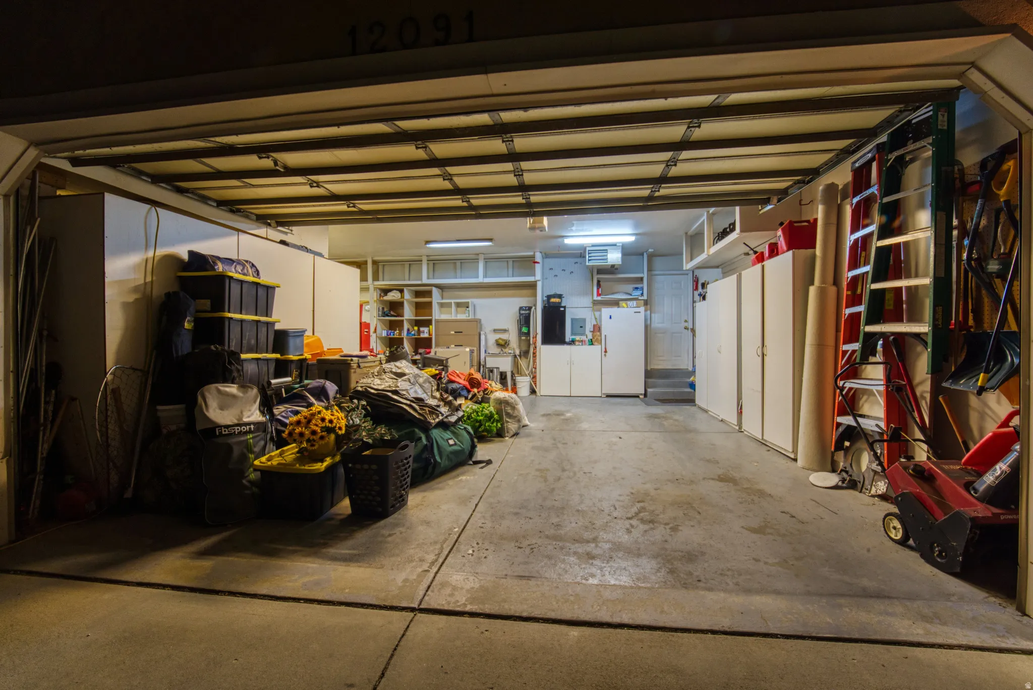 Garage interior featuring a concrete floor, built-in cabinetry, overhead fluorescent lighting, and a roll-up garage door