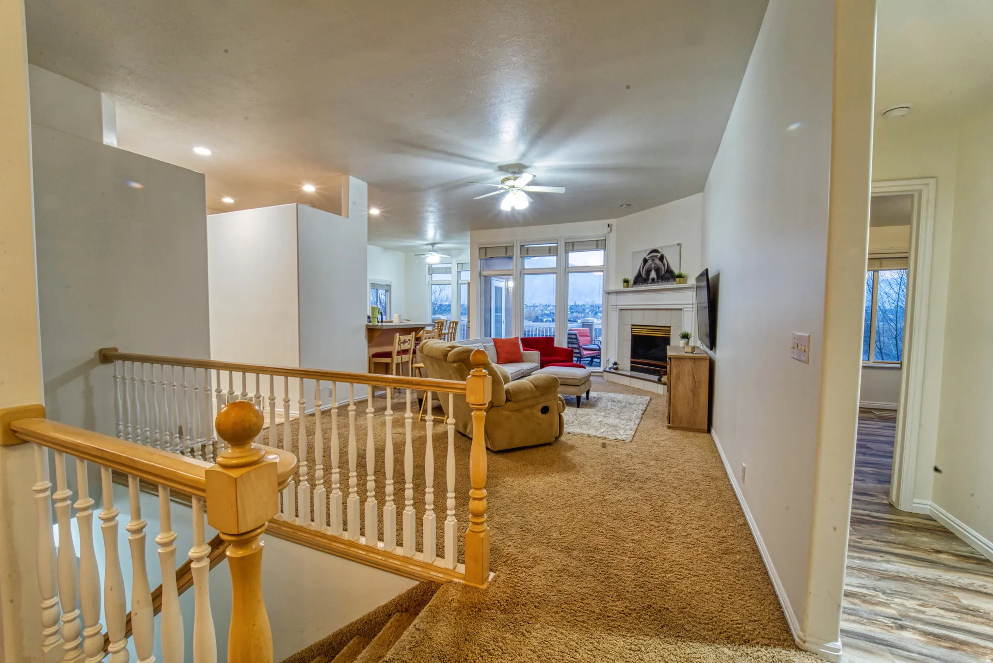 Open-concept living area with carpeted flooring, a white mantel fireplace, and large windows
