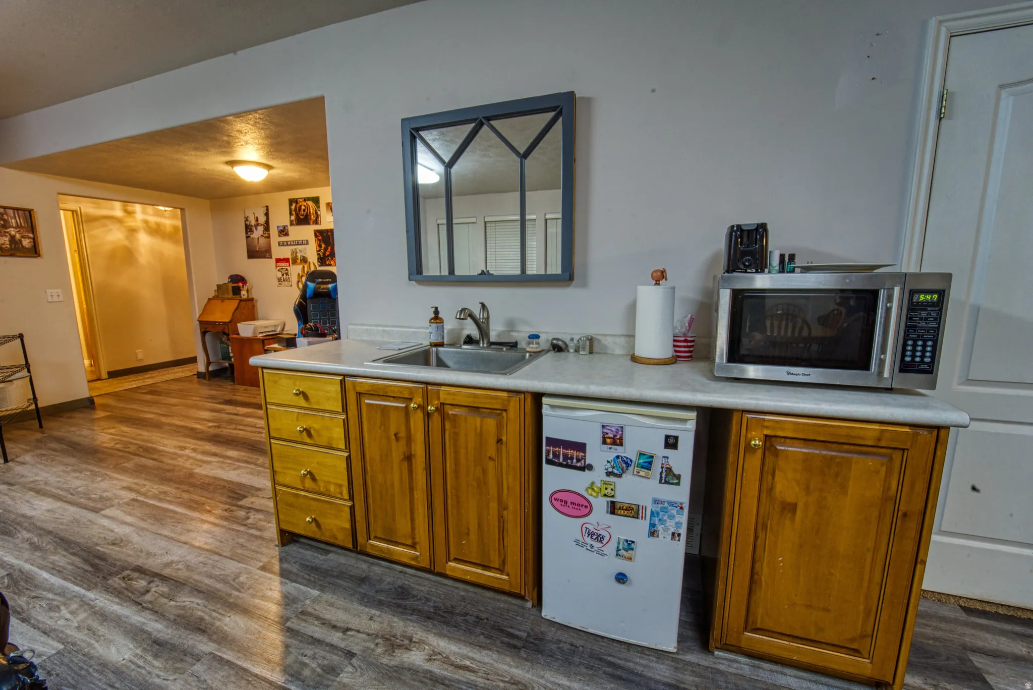 Compact kitchenette featuring a drop-in sink, wood-finish cabinetry, and a light-toned countertop