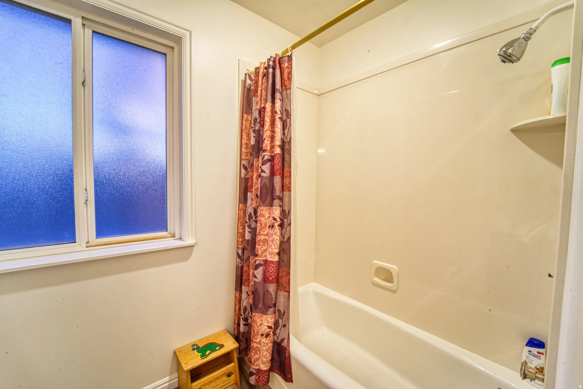 Enclosed bathtub with an integrated shower, featuring a wall-mounted showerhead and a corner shelf
