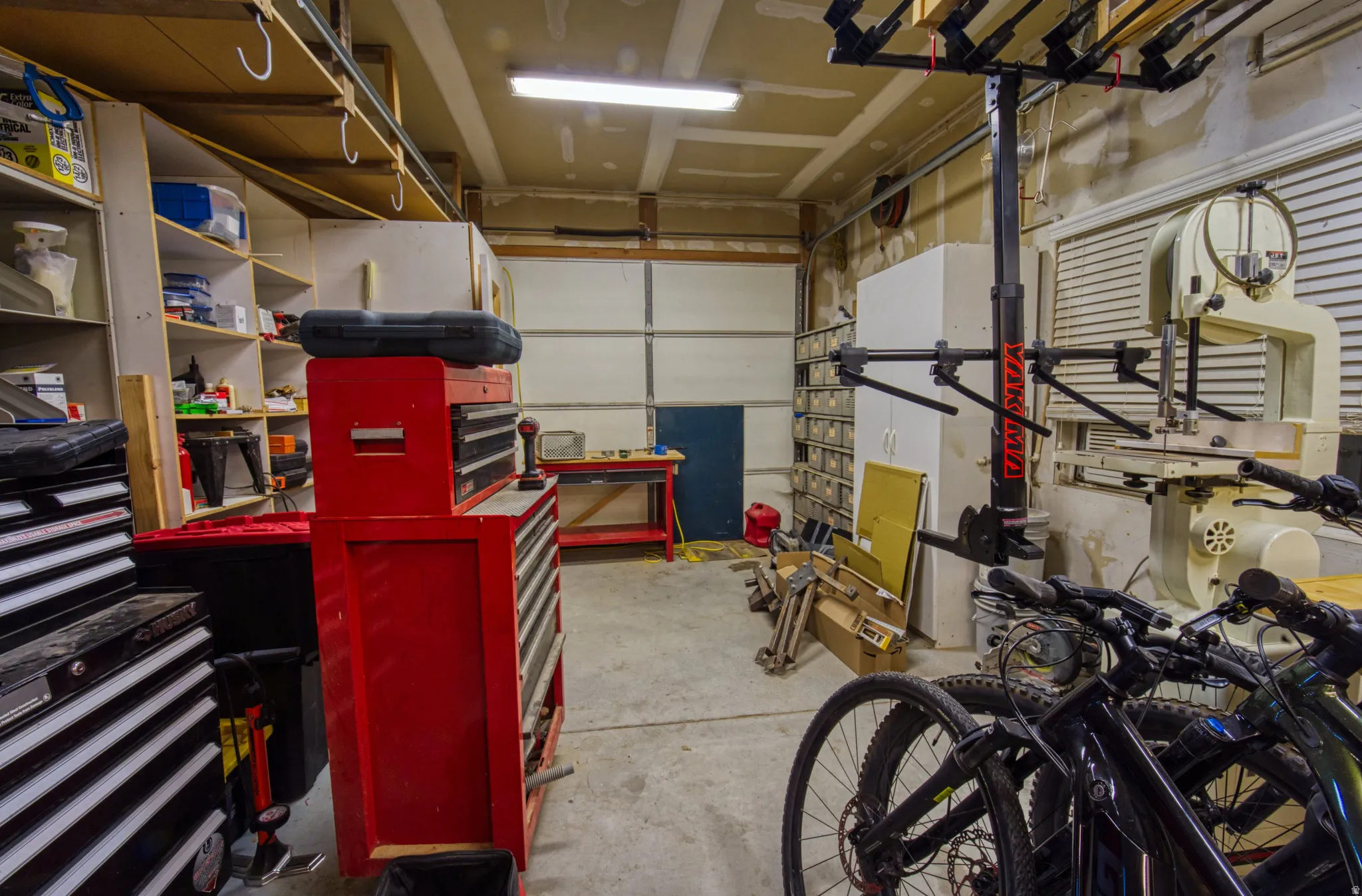 Garage with concrete flooring, fluorescent lighting, built-in shelving, and a roll-up garage door