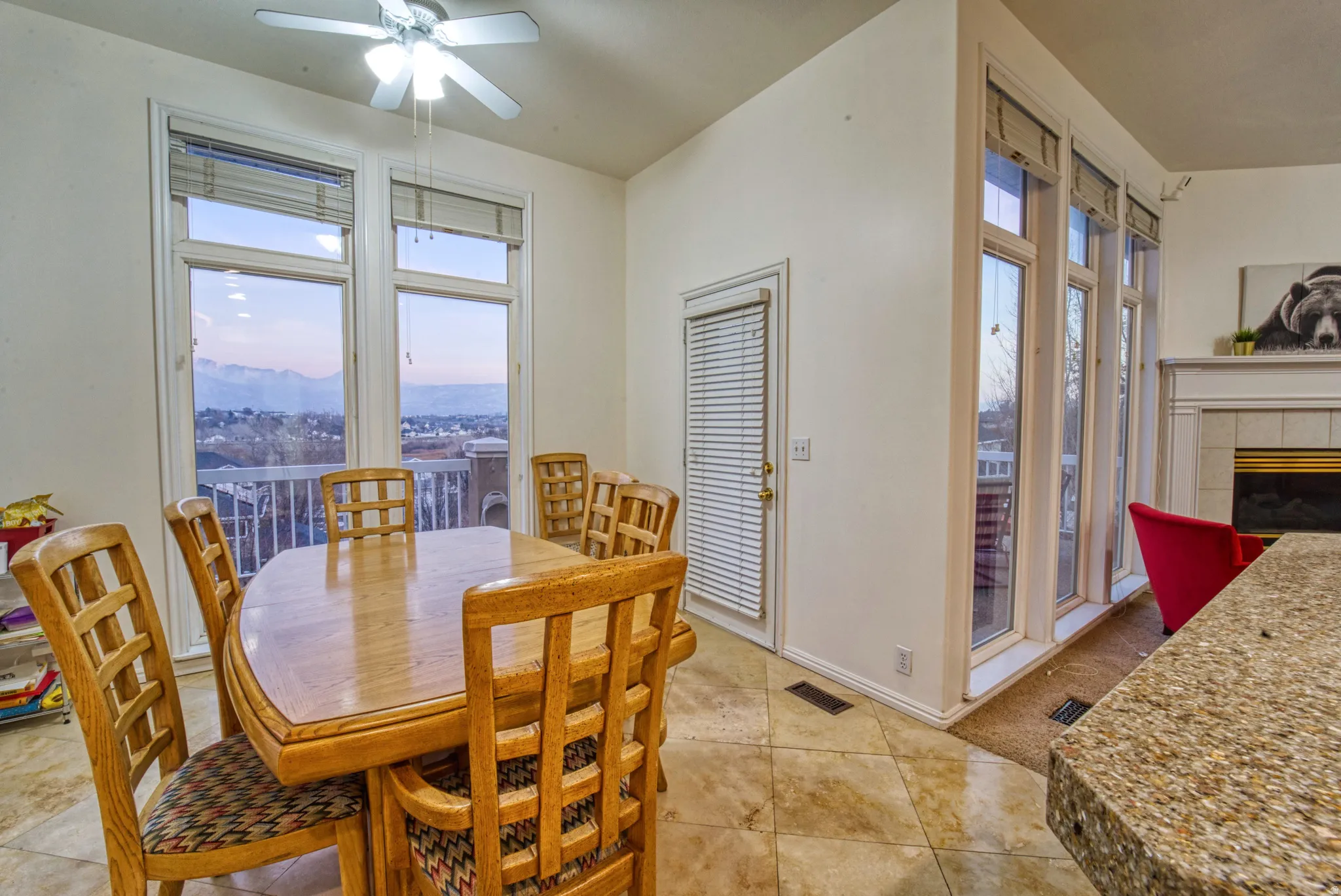 Dining area featuring a ceiling fan, tiled flooring, expansive windows, a door with integrated blinds, and a built-in fireplace with mantel