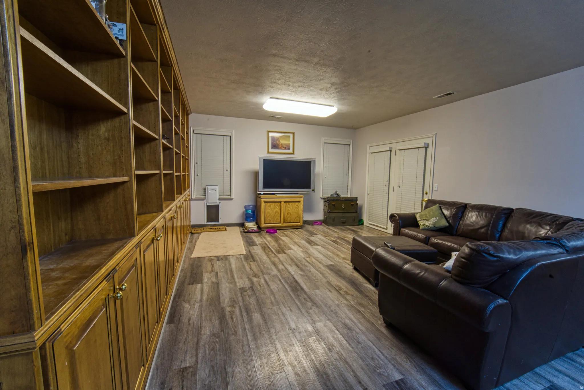 Room featuring extensive built-in wooden shelving and cabinetry, wood-finish flooring, and white walls