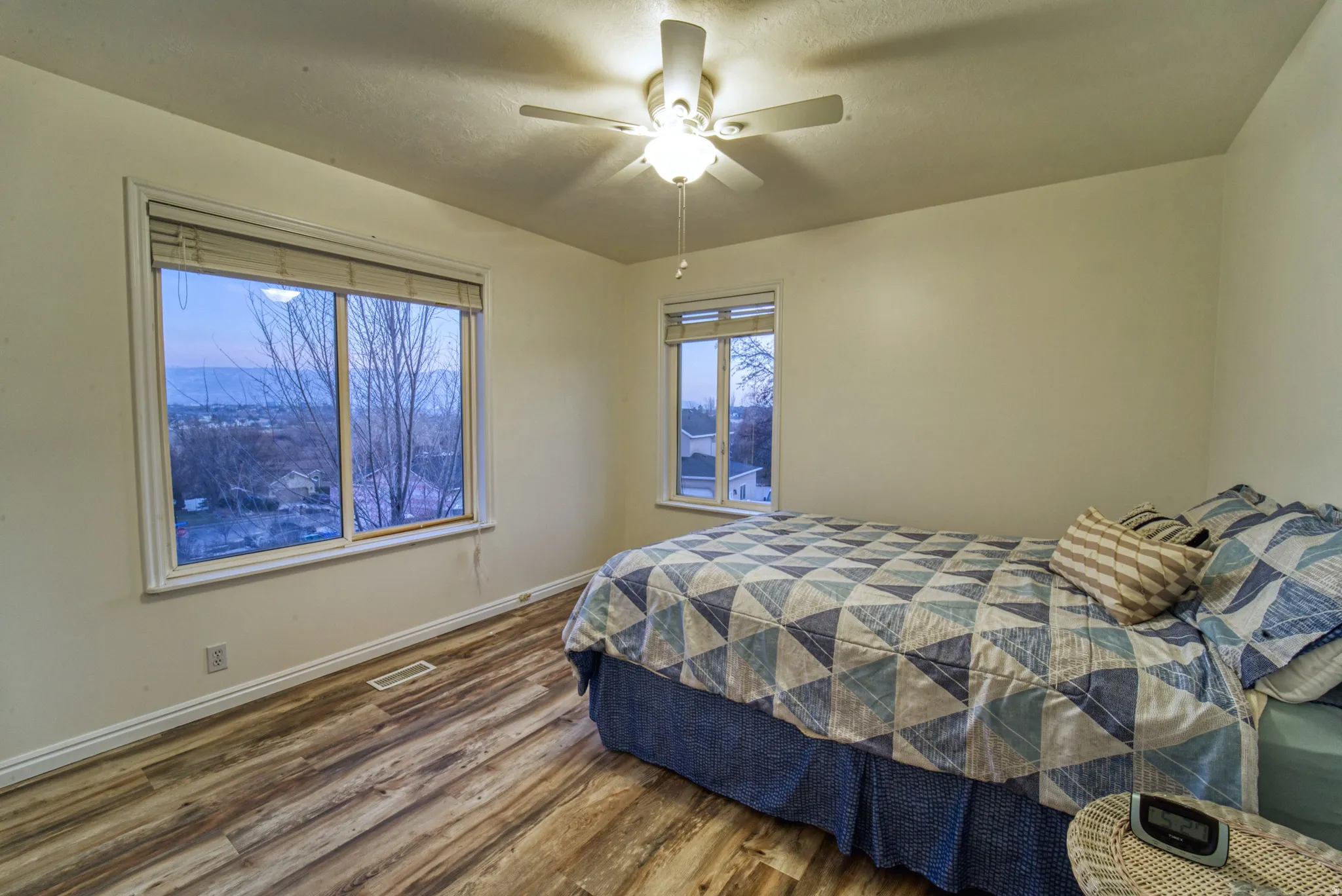 Spacious room featuring wood-finish flooring, a large window, and a ceiling fan with integrated lighting
