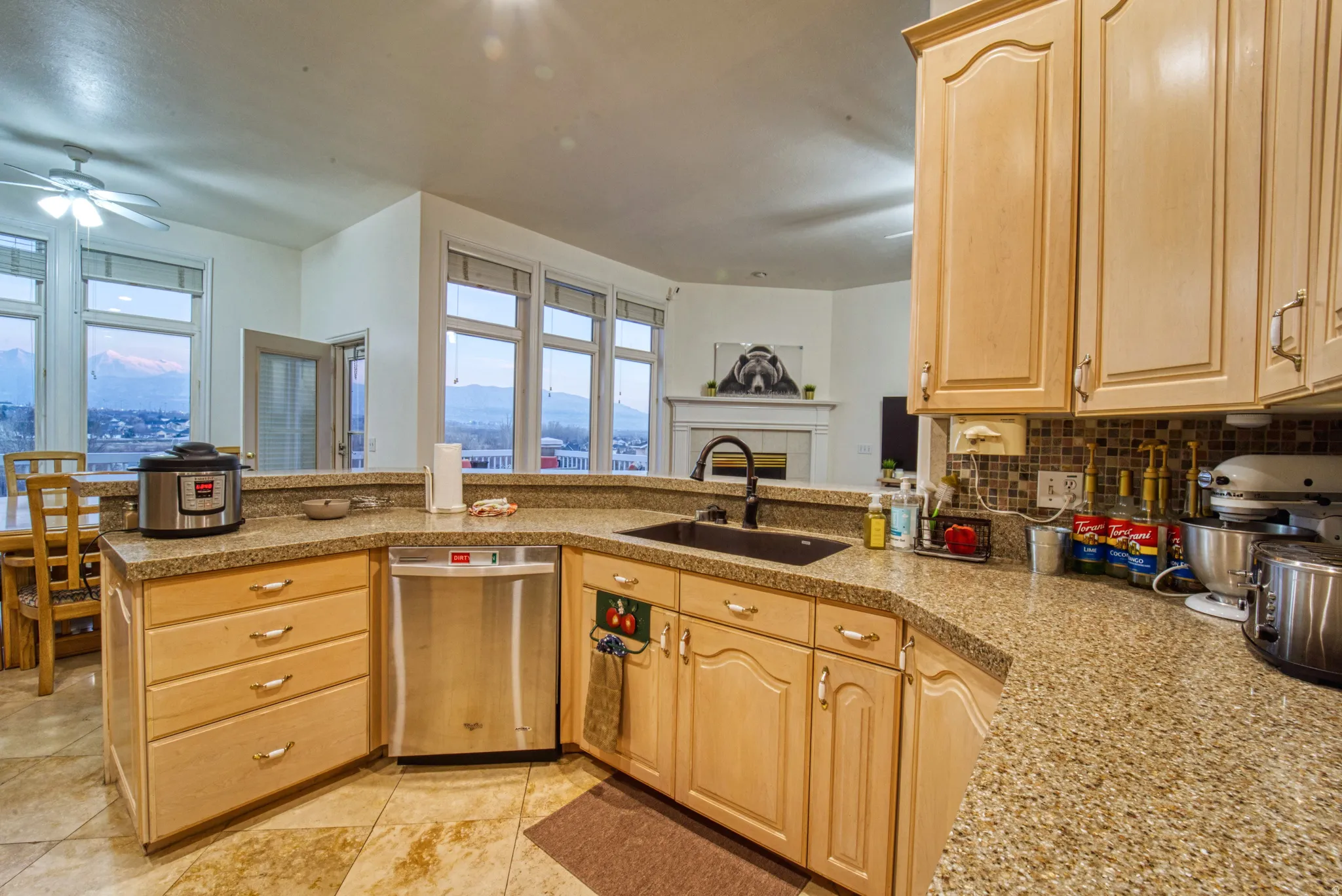 Spacious kitchen featuring light wood cabinetry, stone countertops, a stainless steel dishwasher, and a dark undermount sink with a gooseneck faucet
