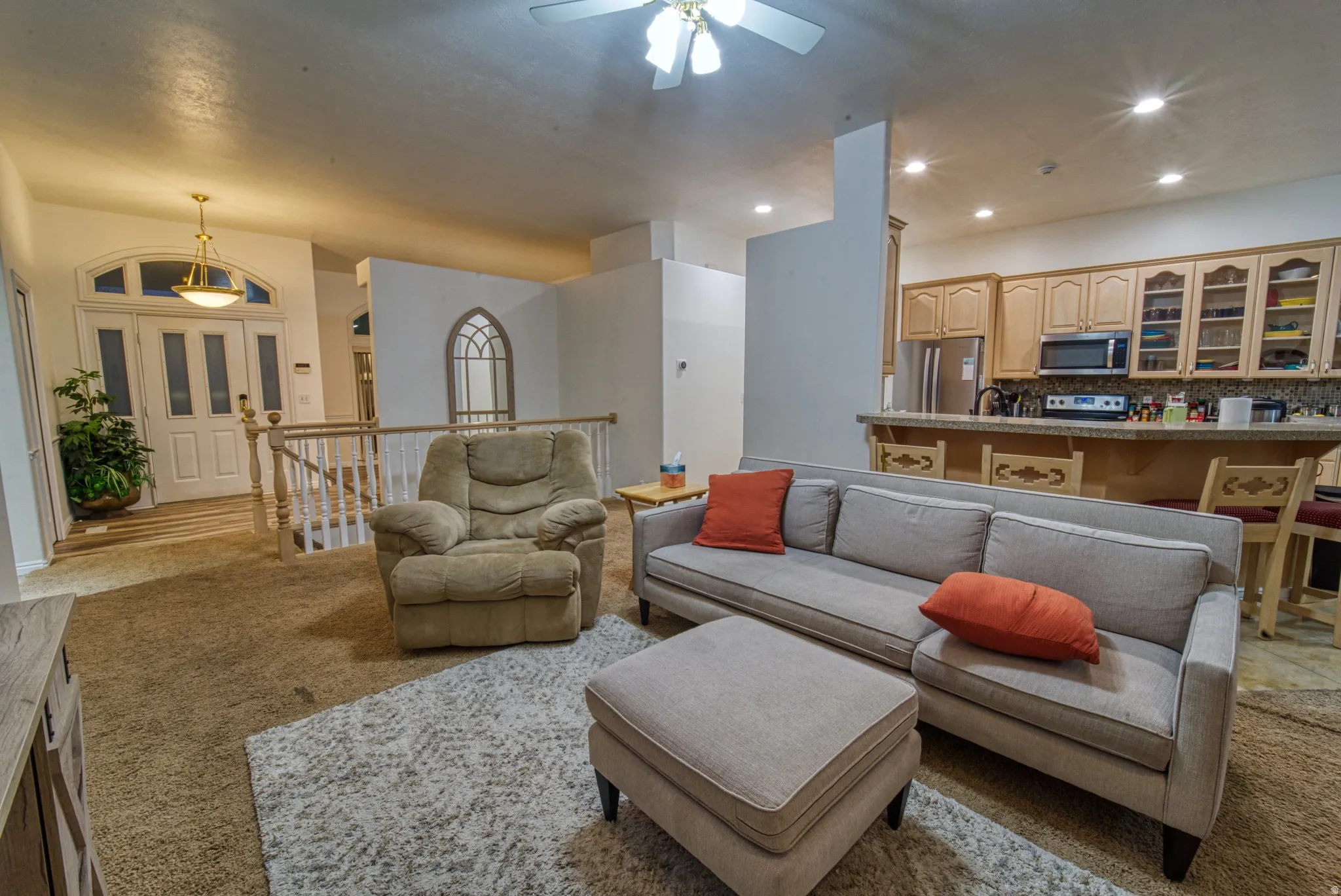 Open-concept living space featuring an arched entryway, staircase with white railings, and a kitchen with warm-toned cabinetry, stainless steel appliances, and a breakfast bar