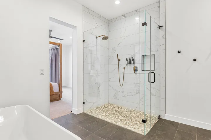 Spacious walk-in shower featuring a glass enclosure, white marble-look tile, and a pebble-stone floor